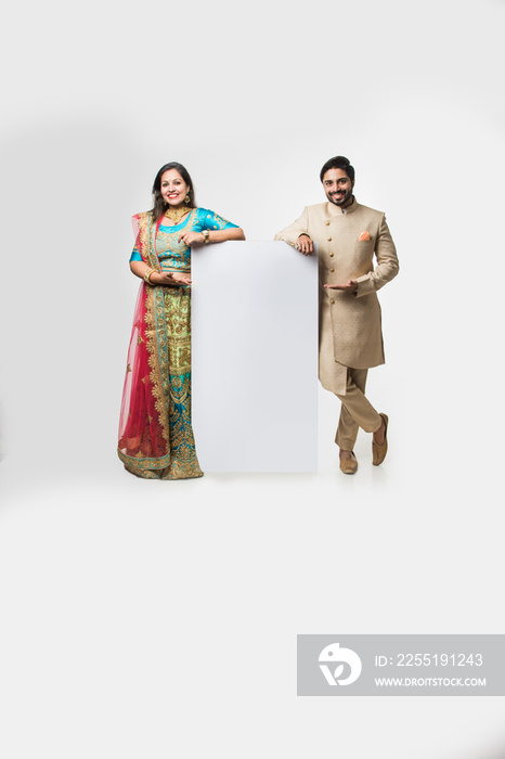 Indian couple holding white board, promoting offers on festival season while wearing traditional cloths, standing isolated over white background