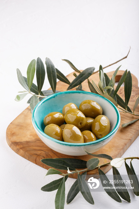 Whole green olives in bowl on white table. Close-up.