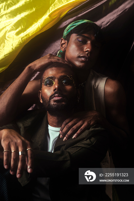 Two Malaysian Indian men in a studio setting with cloth flying in the background, posing against a black bacground