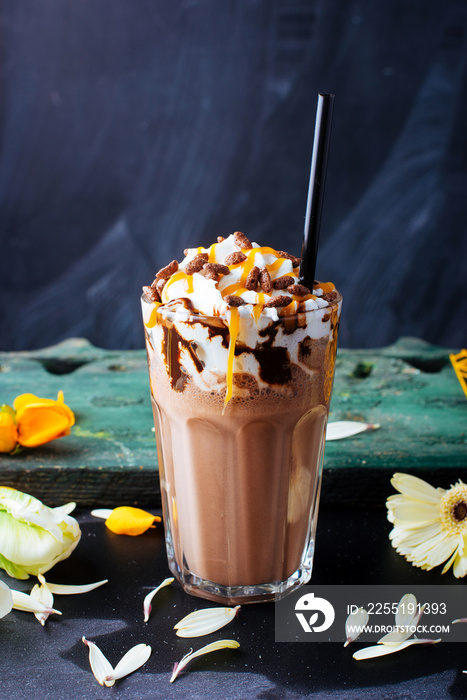 A vertical image of a chocolate milkshake with whipped cream, caramel, chocolate on top on blackbackground.