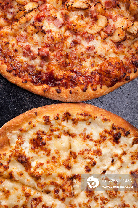 Top view of two pizza lying next to each other on dark wooden background