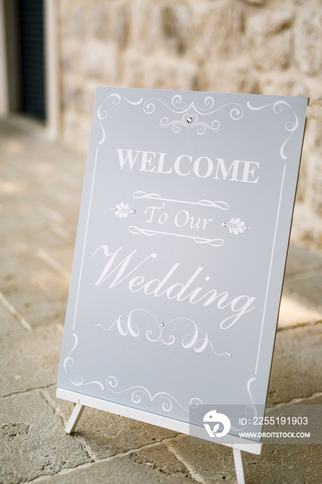 Wooden easel with inscriptions stands in front of an ancient building. Inscription: Welcome To Our Wedding