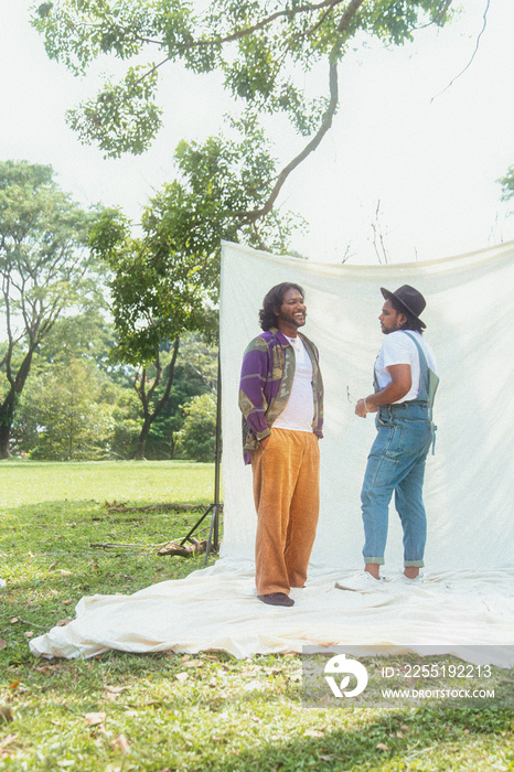 Malaysian Indian men posing and laughing together in a group setting, outdoors, in a park against a cloth backdrop