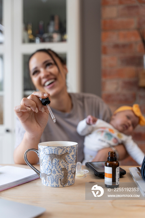 Mother adding vitamins to mug while holding baby girl at home