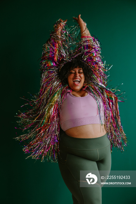 plus size black person with arms in the air wearing a rainbow tinsel jacket