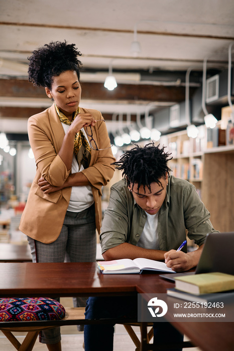 African American professor overseeing her student who is learning in a library.