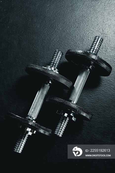 two metallic dumbbells lying on black floor in gym