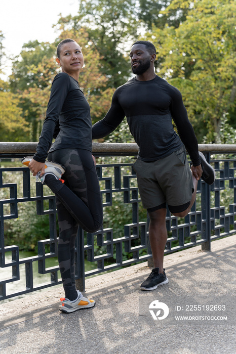 Athletic man and woman stretching legs on bridge in park