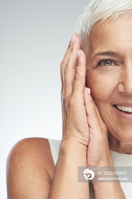 Beautiful smiling senior woman with short gray hair posing in front of gray background. Beauty photography.