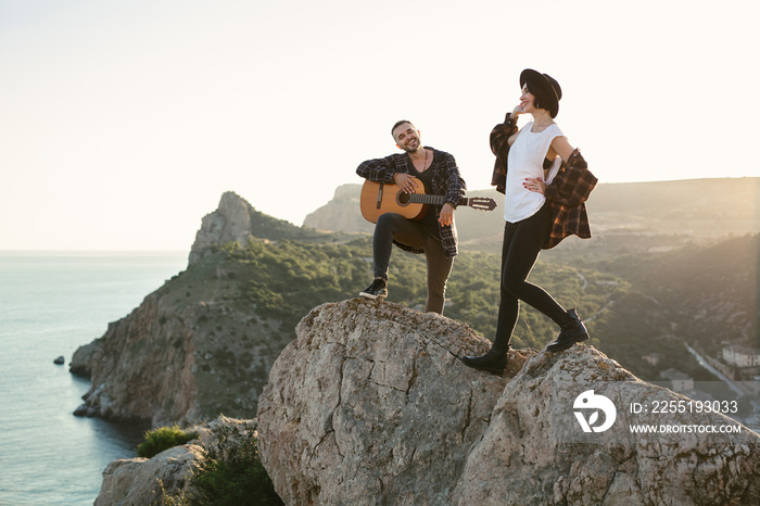 Couple in love on a mountaintop overlooking the sea. Man plays the guitar, a woman dances and sings.