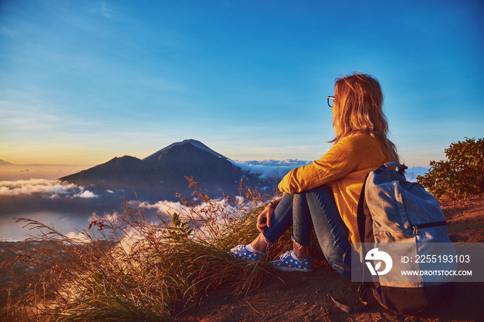 Woman enjoying nice landscape and sunrise from a top of mountain Batur, Bali, Indonesia.