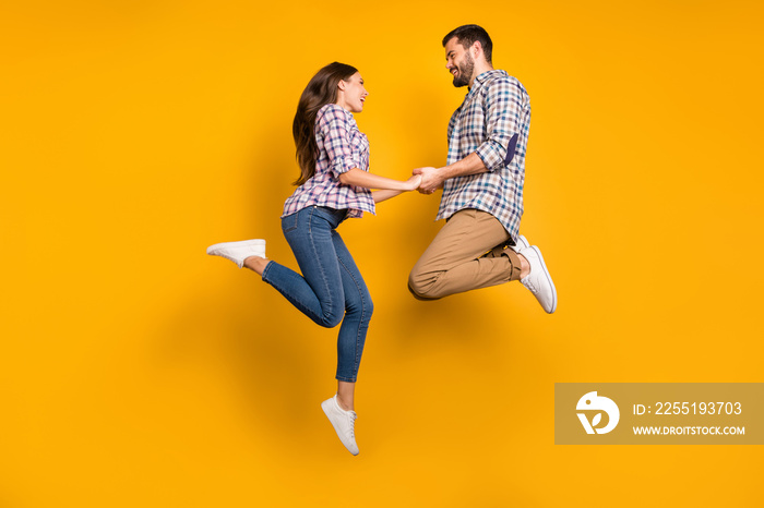 Full body photo pretty lady handsome guy couple jumping high up meet adventures playful holding arms sporty people wear casual plaid shirts jeans pants shoes isolated yellow color background