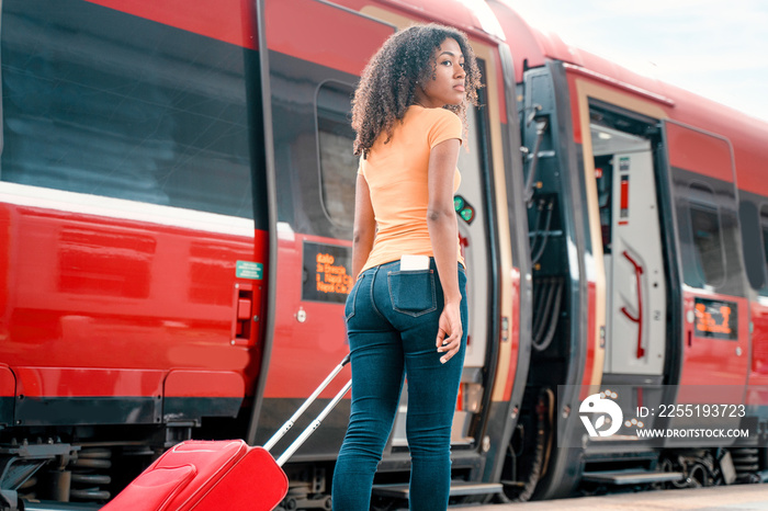 Afro woman ready to take the train with carry on baggage trolley