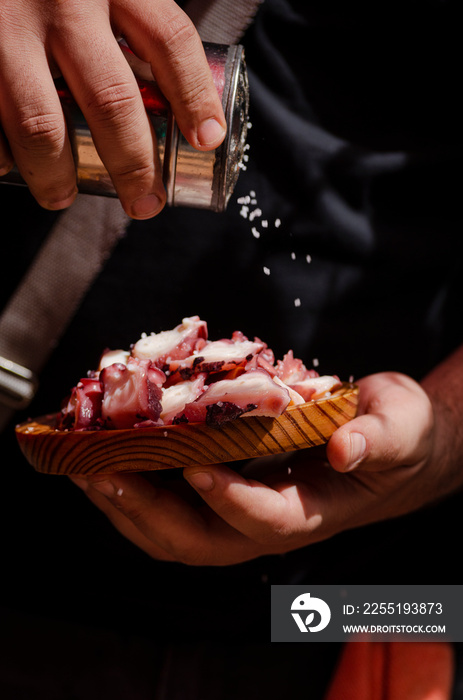 Cook adding salt to a portion of Octopus a Feira, typical Galician recipe for cooking octopus.