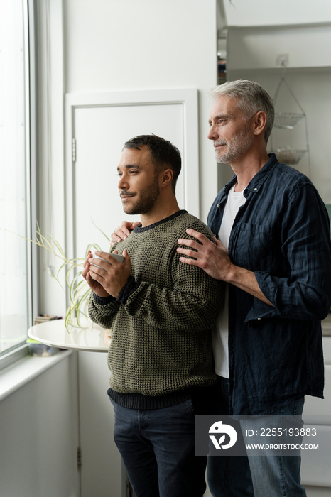 Mature male couple looking through window at home