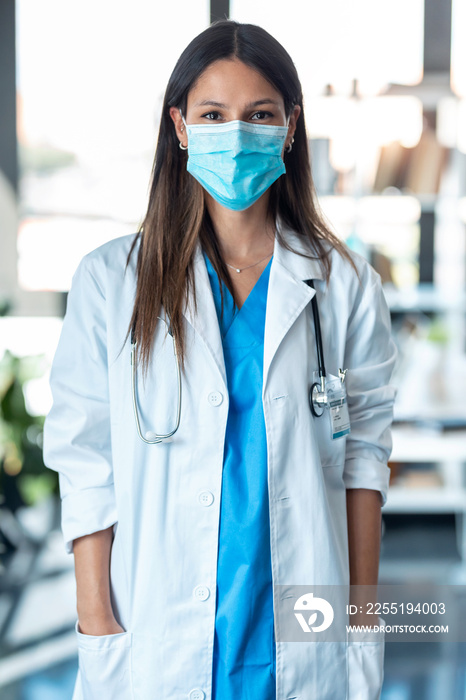 Young female doctor in medical mask looking at camera in the consultation.