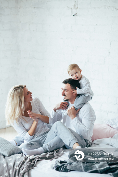 Young family playing and have fun sits on the bed. Mother, father and child. Indoor