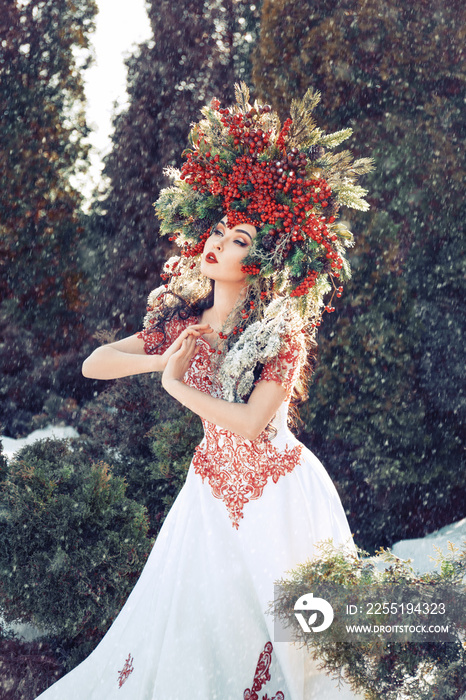 fantasy winter queen standing in the forest in falling snow, a beautiful woman in the crown of red berries and fur branches