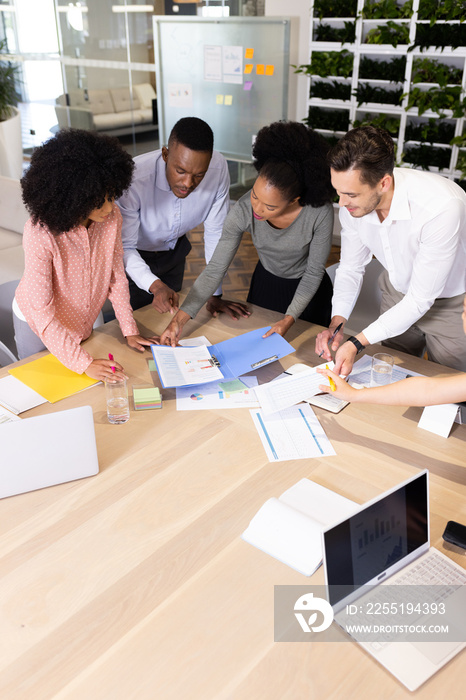 Vertical image of diverse female and male businesspeople talking and working in office