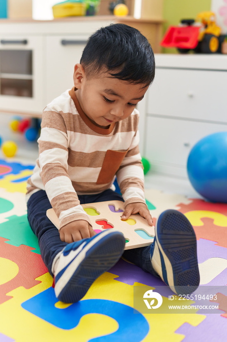 Adorable hispanic toddler playing with maths puzzle game sitting on floor at kindergarten