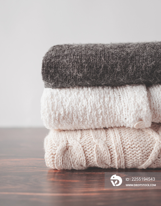 Pile of chunky winter sweaters laying on dark wooden desk or table. Copy space.