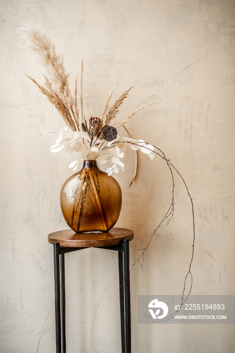 Composition of dried flowers and herbs in a glass vase on a beige wall background. Bouquet of pampas, grass, Cortaderia, nelumbo, banksia, Proteaceae, Eucalyptus, Stabilized plants