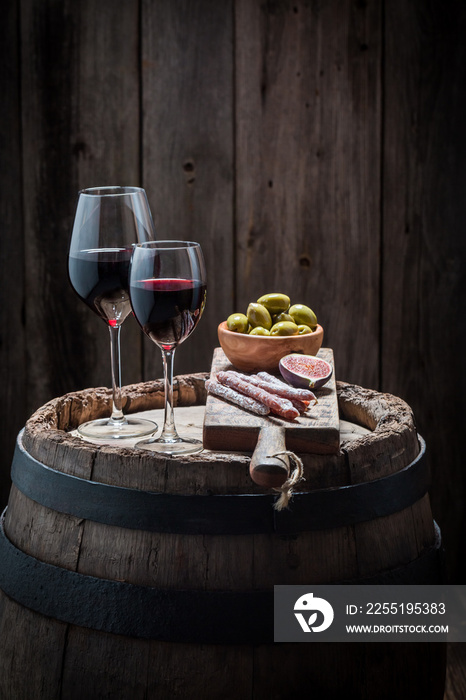 Tasty red wine in glass with olives and cold meats on wooden barrel