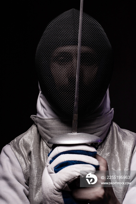 Portrait of male fencer in mask and foil performing fight in studio, dark key