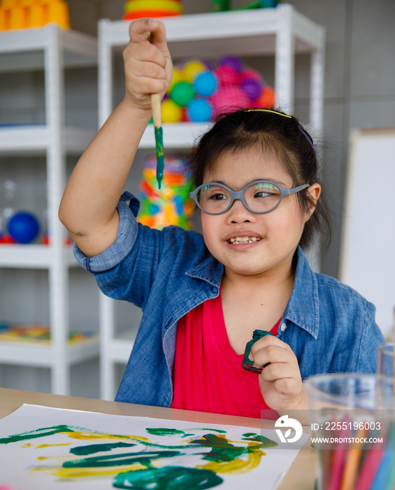 From above happy Asian girl with Down syndrome smiling and showing green gouache  in art classroom