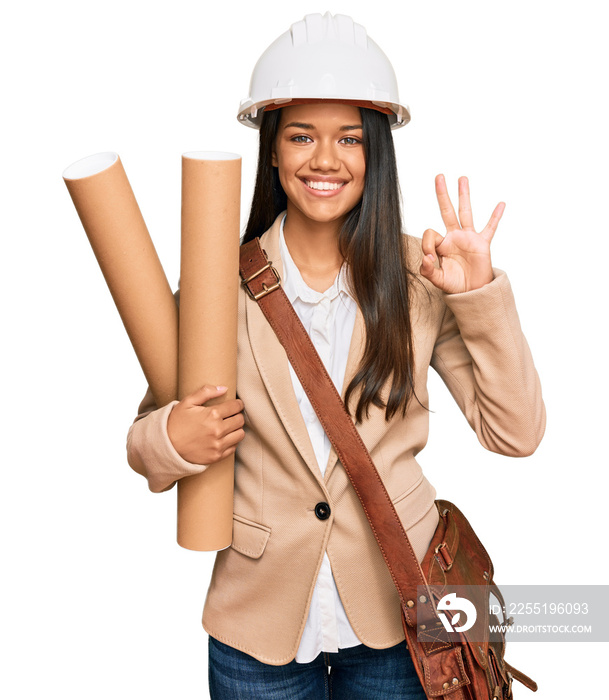 Beautiful hispanic woman holding paper blueprints doing ok sign with fingers, smiling friendly gesturing excellent symbol