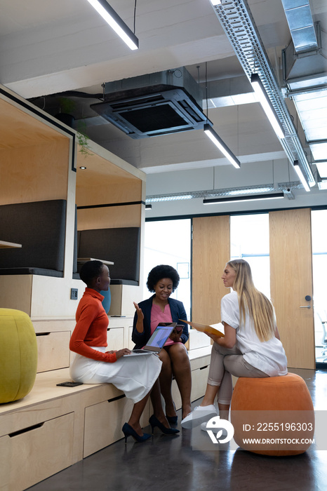 Diverse group of female business colleagues in discussion holding documents using tablet and laptop