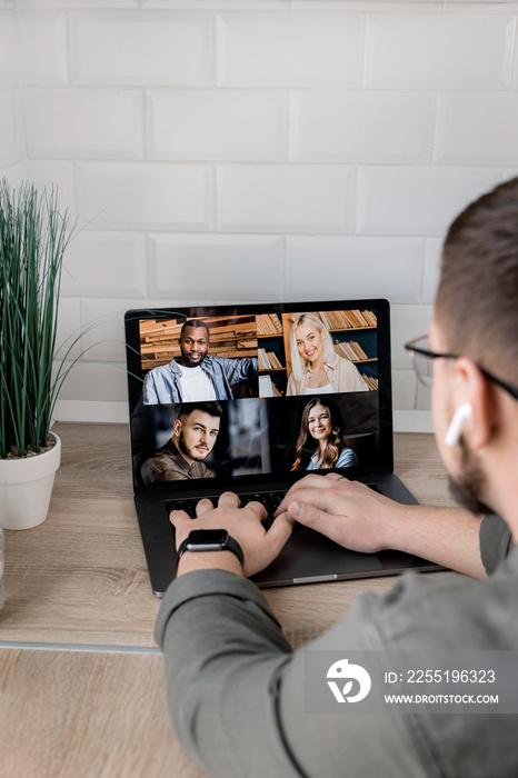 Back view of stylish male employee having an online conference with colleagues, using a laptop. Young businessman discussing corporate project with coworkers by video call, internet meeting concept