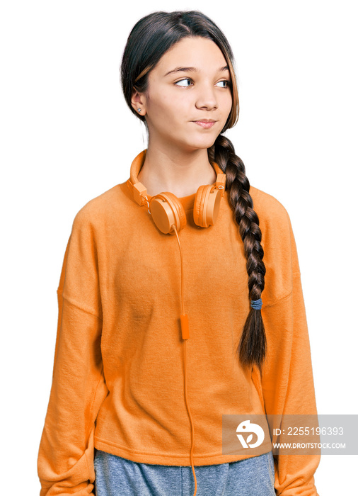 Young brunette girl with long hair wearing sweatshirt and headphones smiling looking to the side and staring away thinking.