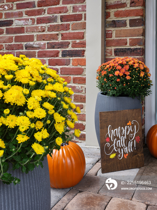 Colorful flowering mums and orange ceramic pumpkins on a beautiful warm tones of paver bricks on the front porch of an american home