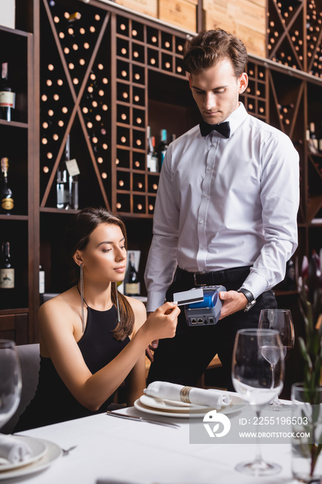 Selective focus of elegant woman paying with credit card to waiter in restaurant