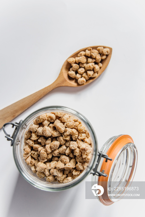 Vista superior de una cuchara de madera y un tarro de cristal lleno de habas de soja texturizada gruesa. Concepto de alternativas veganas a la carne. Proteína vegetal. Cocina vegetariana.