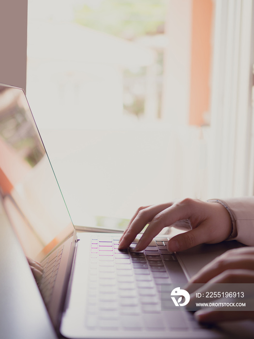 close up on right hand of business woman(30s to 40s) with pink or pastel suits working at home office with her computer laptop with soft focus left hand and foreground keyboard