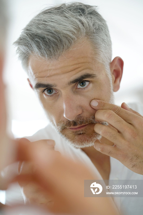 Middle-aged man applying cosmetic on his face, mirror view