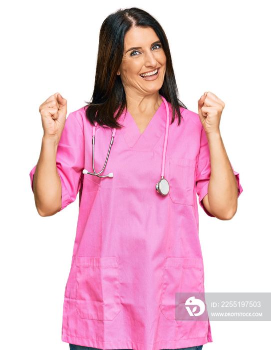 Middle age brunette woman wearing doctor uniform and stethoscope screaming proud, celebrating victory and success very excited with raised arms