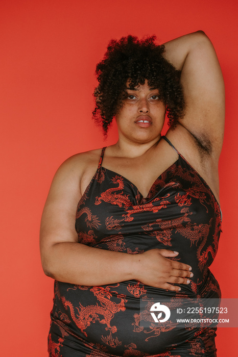 portrait of a plus size afro indigenous person looking at camera on red backdrop