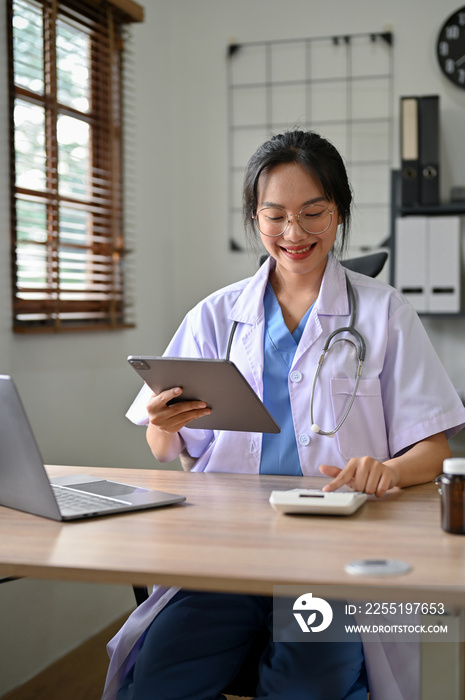 Beautiful Asian female doctor using calculator, estimating surgery cost for her patient