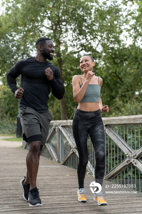 Smiling athletic couple jogging on footbridge in park