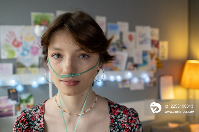 Brunette teenage girl with oxygen nose pipe standing in front of camera in hospital ward during course of therapy