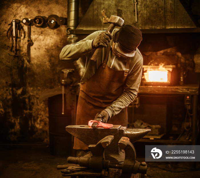 The blacksmith forging the molten metal on the anvil in smithy