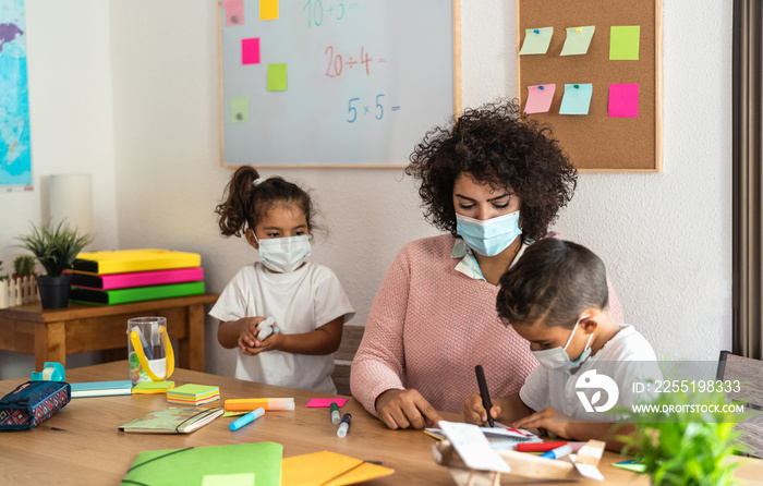 Teacher with children drawing in preschool classroom while wearing face protective mask during corona virus pandemic - Healthcare and education concept