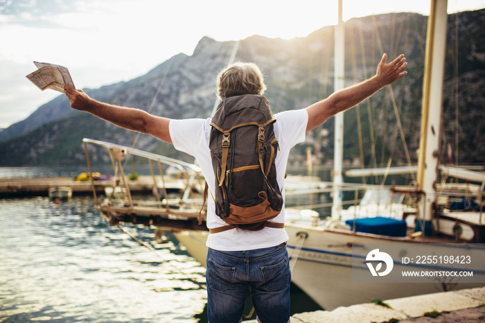 Smiling tourist mature man standing with map and backpack near the sea.