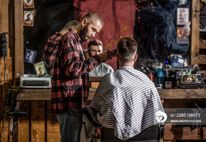 Bearded man in barbershop. Haircut concept. Man visiting hairstylist in barbershop. Barber works with hair clipper. Hipster client getting haircut. Hands of barber with hair clipper, close up