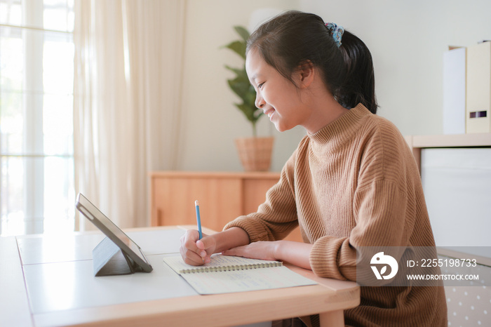 Asian kid studying online using tablet in a living room alone.