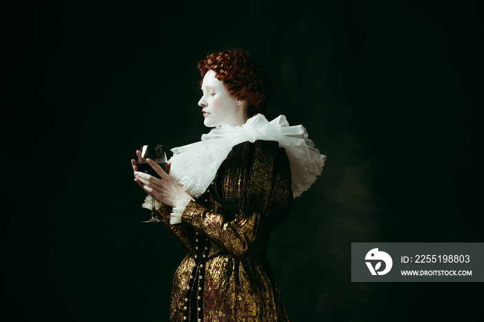 One part of me. Medieval redhead young woman in golden vintage clothing as a duchess holding a glass with red wine on dark green background. Concept of comparison of eras, modernity and renaissance.