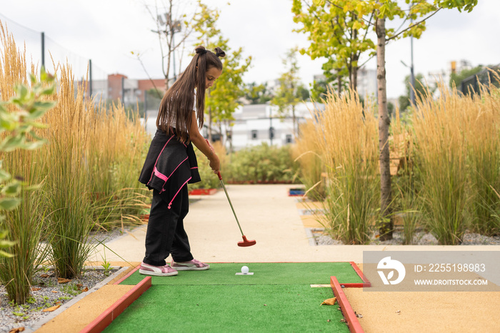 Miniature golf outdoor. Little caucasian girl golfing in the mini golf course.